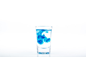 Blue food coloring diffuse in water inside shot glass with empty copyspace area for slogan or advertising text message, over isolated white background.
