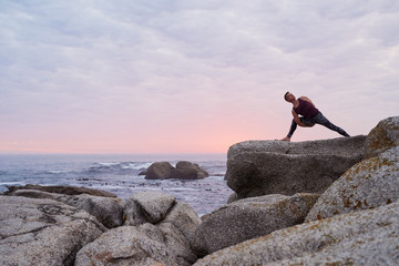 Man doing the eight angle pose on a rocky coastline