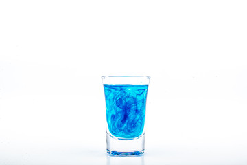 Blue food coloring diffuse in water inside shot glass with empty copyspace area for slogan or advertising text message, over isolated white background.