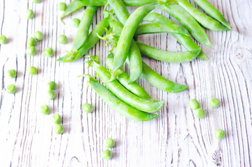 Young peas in pods and without on a light wooden background.