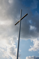 Large metal cross with blue sky and white clouds in the background