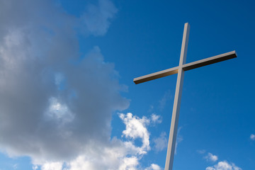 Large metal cross with blue sky and white clouds in the background