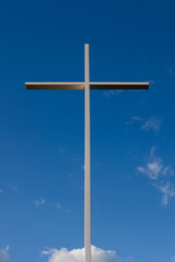 Large metal cross against blue sky background with parts of white clouds