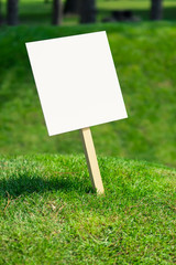 Empty white sign board on a small hill with freshly cut green grass and meadow in the background