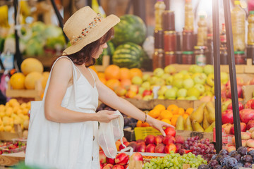 Young Woman puts fruits and vegetables in cotton produce bag at food market. Reusable eco bag for...