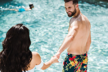 Fototapeta premium selective focus of happy man and woman holding hands near swimming pool