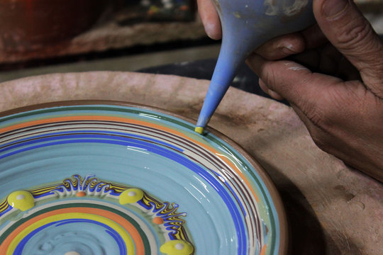 The Master Potter, A Ceramist With 13 Years Of Experience, Decorates A Clay Plate Made On A Pottery Wheel Using Colored Engobes. National Method Bulgarian Flyandrovka.