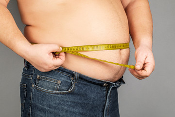 A man measures his fat belly with a measuring tape. on a gray background.