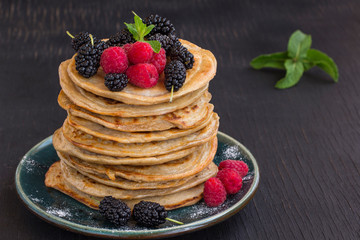 Delicious pancake with blackberries, raspberries and icing sugar in dish on black table.
