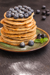 Delicious pancake with blгуberries, and icing sugar in green dish on black table.
