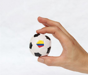 Fototapeta premium Mini ball of football in hand and one black point of football is Colombia flag, hold it with two finger on white background. Concept of sport or the game in handle or minor matter.