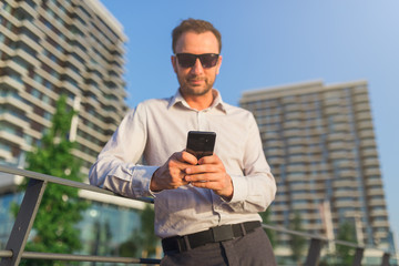 Young caucasian business executive holding smartphone for business work outdoors.