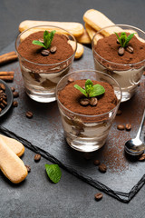 Classic tiramisu dessert in a glass and savoiardi cookies on stone serving board on dark concrete background