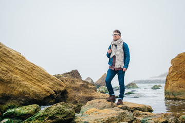 Man traveler with a backpack standing on a rock against a beautiful sea with waves, a stylish...