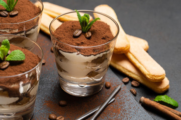 Classic tiramisu dessert in a glass and savoiardi cookies on stone serving board on dark concrete background