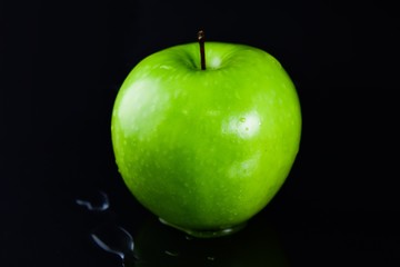 Close up a green apple has water droplets on the floor and has a black background
