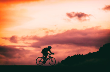 Road racing bike cyclist riding at night . Silhouette of male athlete training at sunset background.