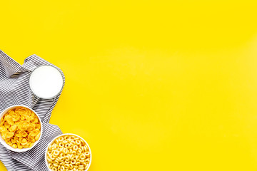 cereals, oatflakes and cornflakes with milk and towel for healthy breakfast on yellow background top view mock up