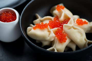 Close-up of vareniki or dumplings with cottage cheese and red caviar served in a black bowl, horizontal shot