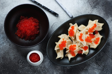 Vareniki with cottage cheese stuffing and red caviar, flatlay over grey stone background, horizontal shot
