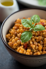 Fregola pasta with bell pepper, capers and green basil, closeup, selective focus