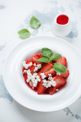 White plate with strawberry dessert, elevated view over white concrete background, vertical shot