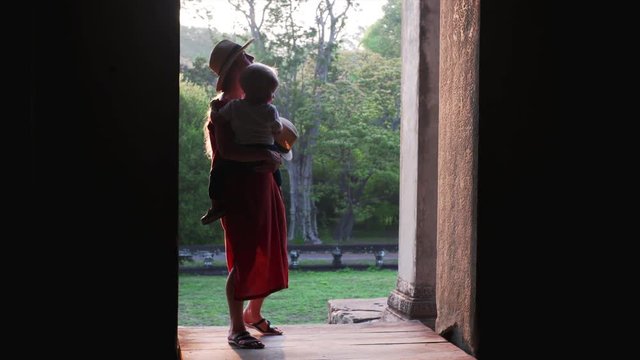 Caucasian mother with cute son is entering Angkor Wat temple and exploring ancient bas-reliefs on the wall. Cambdia