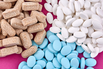 Blue, brown and white pills on pink background