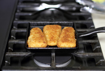 Fish sticks baked on a raclette pan resting on the stove top.