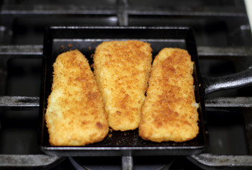 Fish sticks baked on a raclette pan resting on the stove top.