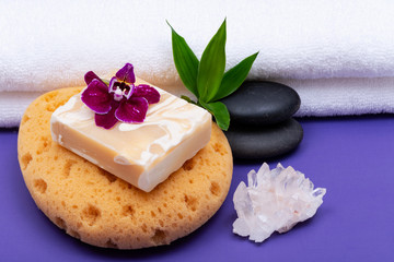Fototapeta na wymiar Spa Wellness Concept. Natural Foam Sea Sponge, Goat milk Soap, Basalt Stones, Bamboo, Orchid and Himalayan Clear Quartz Cluster on purple background.