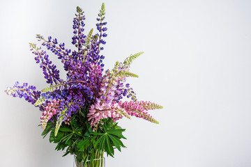 A large bouquet of colorful wild flowers of the lupine in a glass vase. Isolated on white...