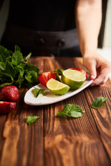 lime strawberry mint ingredients for making lemonade on white plate on wooden table