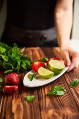 cooking of cooling summer cocktail with strawberries, ice and mint and around the berries are ripe fresh strawberries and lime