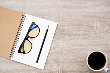 top view glasses and pencil place on open blank book,and coffee cup on wooden table.