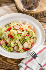 Plate of healthy green garden salad with fresh vegetables on white plate on wooden table