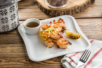 Grilled shrimp on skewer and lemon on white plate on wooden table