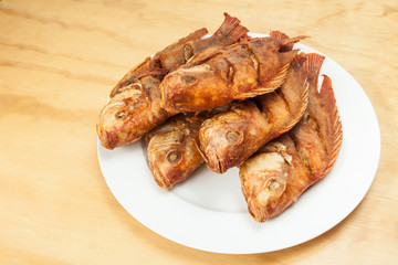 Tasty fried fish, tilapia on a white plate; photo on wooden background
