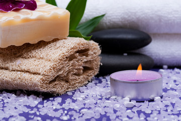 Spa Wellness Concept. Natural Loofah Sponge, Almond Goat milk Soap, Basalt Stones, Bamboo, Orchid and Lavender Tea Light Candle on purple background.