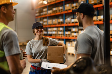 Happy female warehouse worker talking with her coworkers.