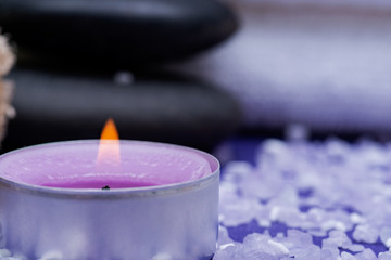 Spa Wellness Concept. Natural Loofah Sponge, stacked Basalt Stones, burning Lavender Tea Light Candle and sprinkled Epsom Salt on purple background.