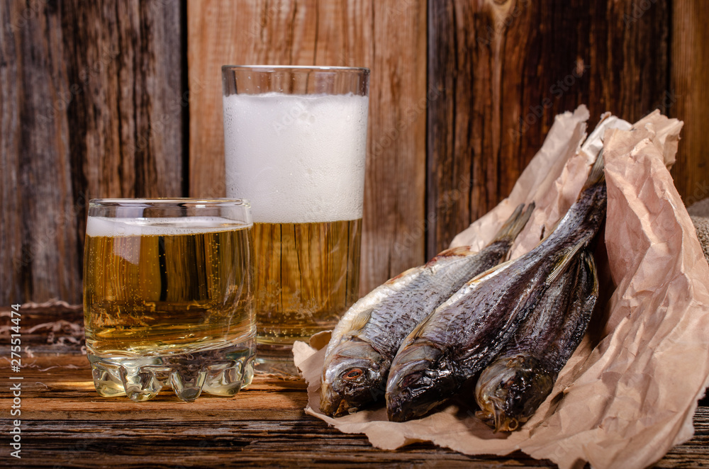 Wall mural Beer in a glass next to dried fish on a wooden background