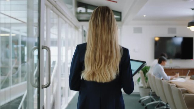 rear view blonde business woman walking through office holding tablet computer enjoying successful leadership career in corporate workplace 4k  