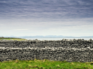 Traditional dry stone fences. Ocean and calm blue cloudy sky in the background. Mason craft example. West of Ireland. Irish landscape. 
