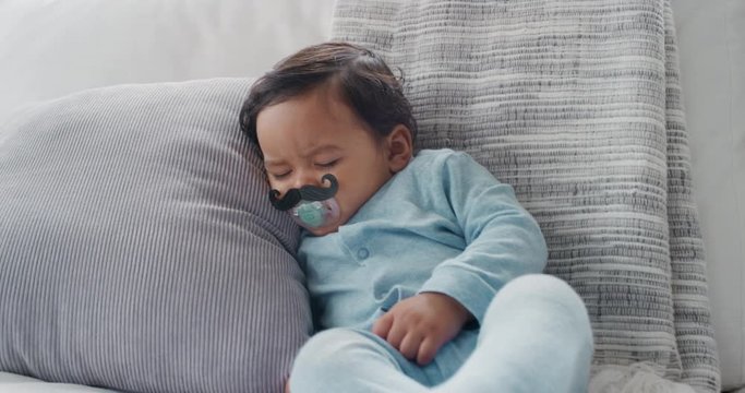 funny baby sleeping with moustache pacifier sucking on dummy at home movember concept