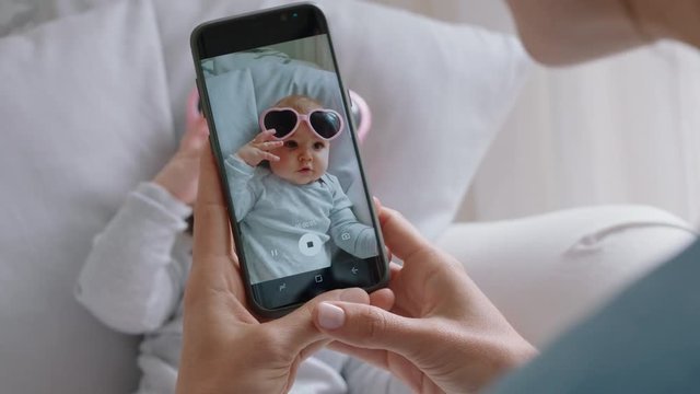 mother taking photo of funny baby wearing sunglasses using smartphone enjoying photographing cute toddler sharing motherhood lifestyle on social media