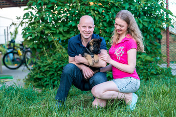 Young happy couple with a funny puppy of a German shepherd. A girl and a guy on a green lawn near the house with a new dog. Buying a pet. The joy of first meeting. Copy spase