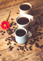 Black coffee In the cup sky blue color 1 and white 2 Have all 3, cups have roasted coffee beans are on table with, still have red flowers all placed on a wooden table.