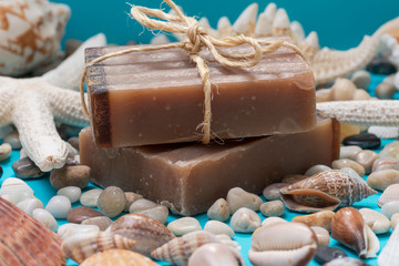 Handmade moisturizing Frankincense & Myrrh Goat's Milk Bar Soap decorated with small Pebbles, Sea Stars and Sea Shells on bright blue background.