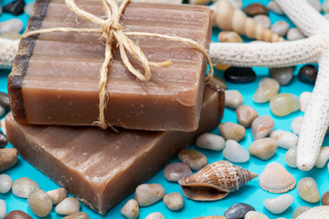 Handmade moisturizing Frankincense & Myrrh Goat's Milk Bar Soap decorated with small Pebbles, Sea Stars and Sea Shells on bright blue background.